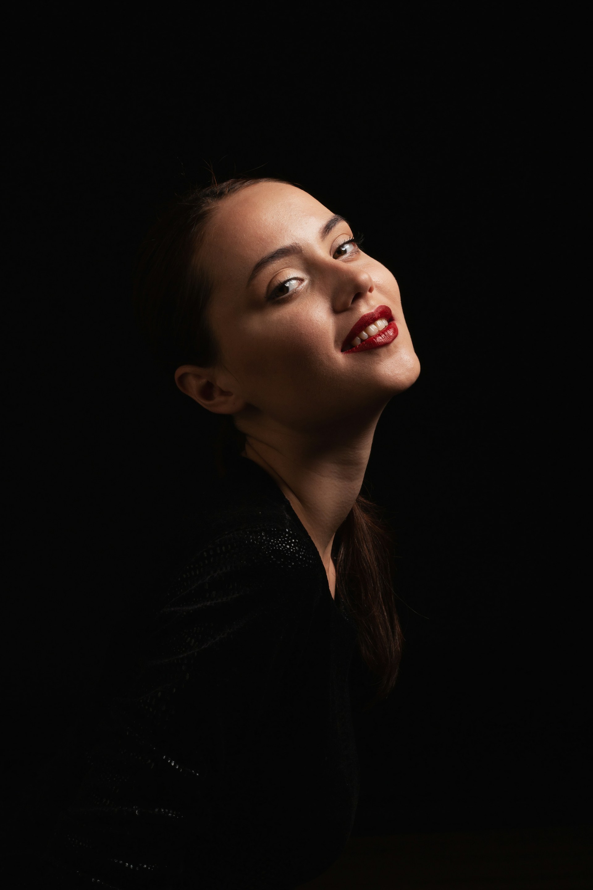 Portrait: a woman with her hair tied back and dark red lipstick, lit against a black background